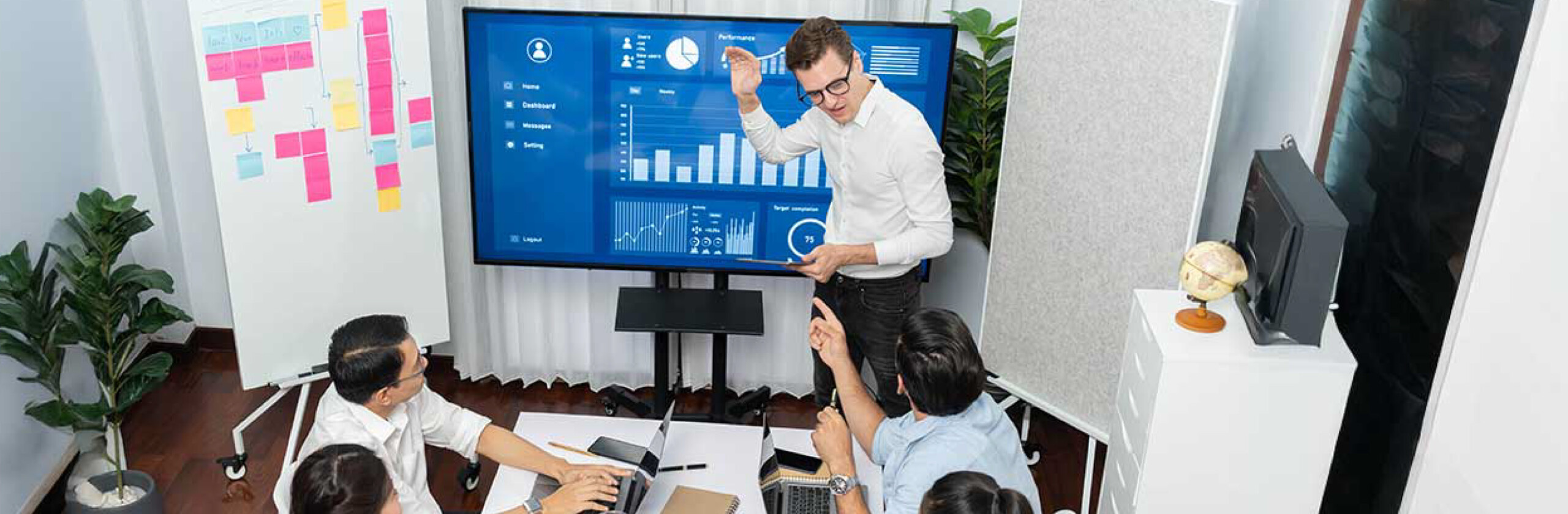 Team gathered in a conference room while a presenter explains project data on a screen with charts and graphs.