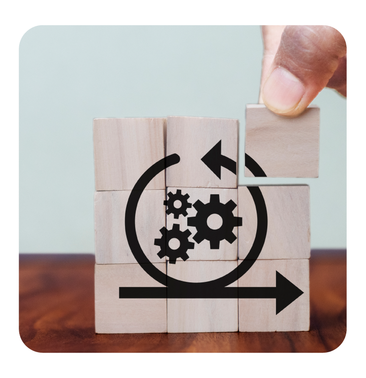 A hand places a wooden block to complete stack with agile symbol and gear icons printed on the front.